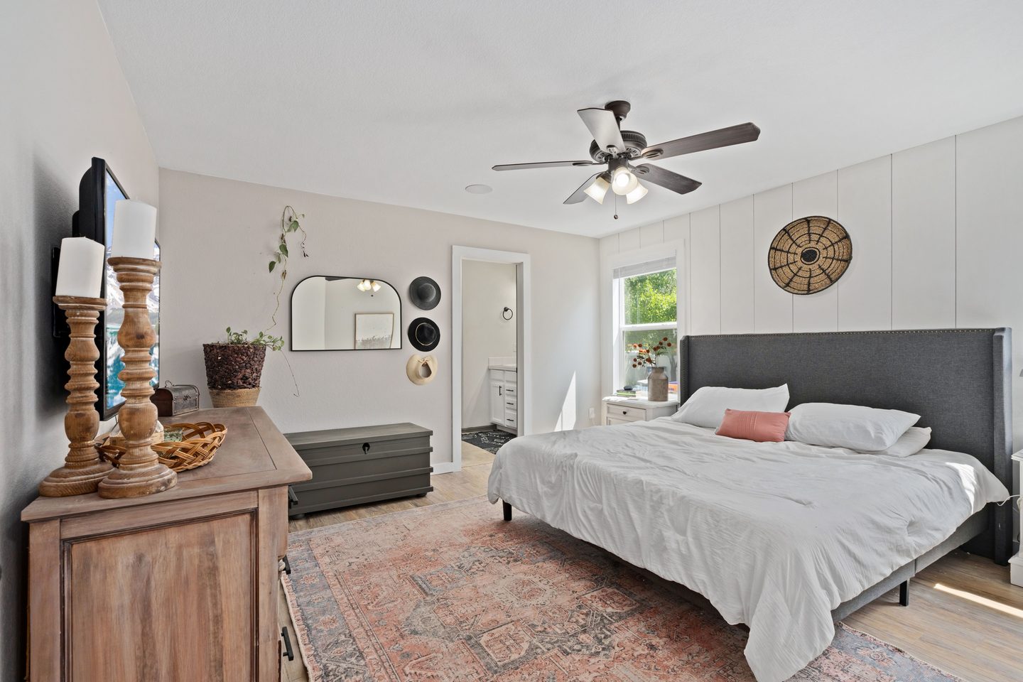 Dormitorio con cabecero gris, cómoda de madera y alfombra